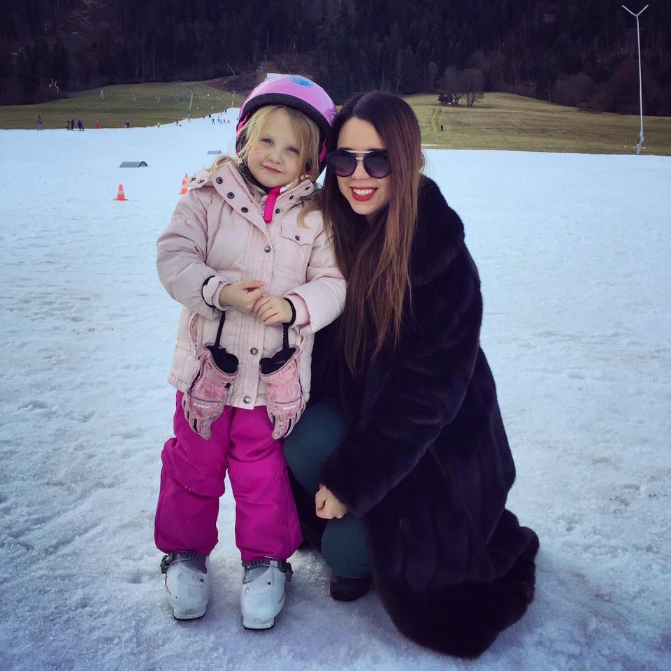 Au pair mexicana junto a una niña con casco de esquí en la nieve